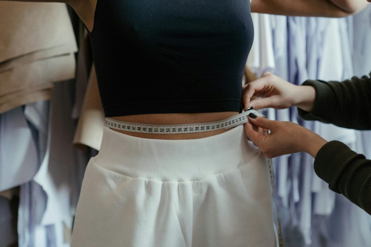 Detailed view of a tailor measuring a client's waist in a clothing workshop, focusing on precision.